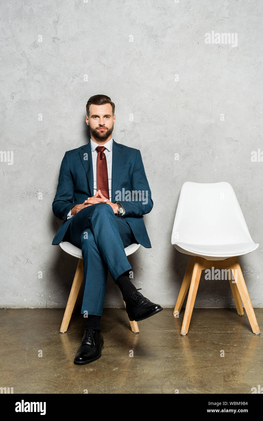 Gut aussehender bärtiger Mann Sitzen mit gekreuzten Beinen auf Stuhl im Büro Stockfoto