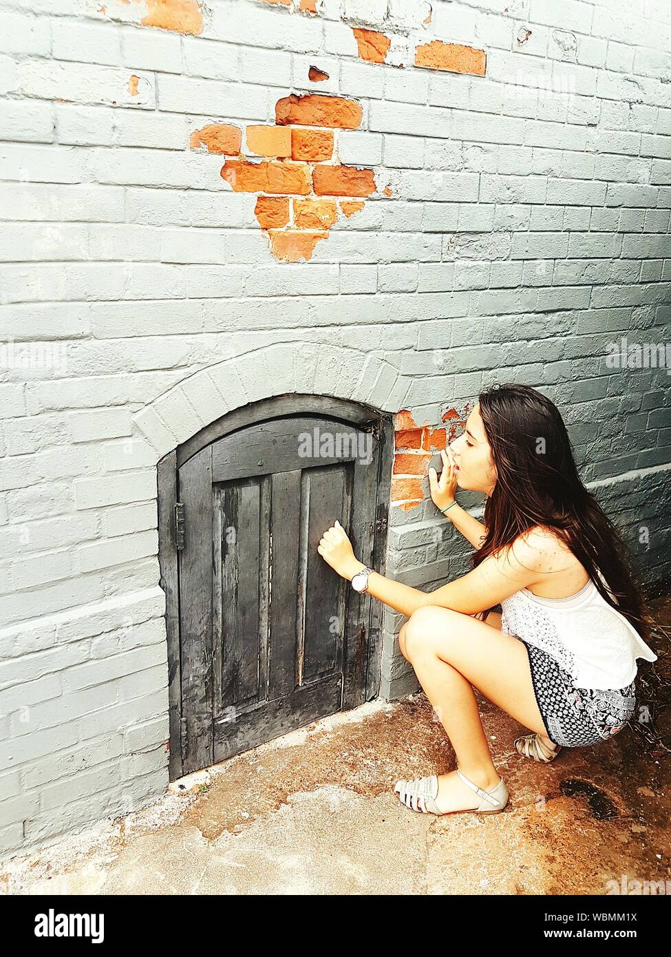 Hohe Betrachtungswinkel von Frau geduckt Durch die Kleine Tür auf der Mauer Stockfoto