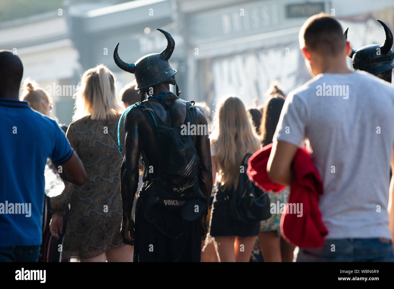Die Rückseite der schwarze Mann mit dem Hut mit Hörnern auf es zu Fuß durch die Menschenmenge in Notting Hill Carnival. Stockfoto