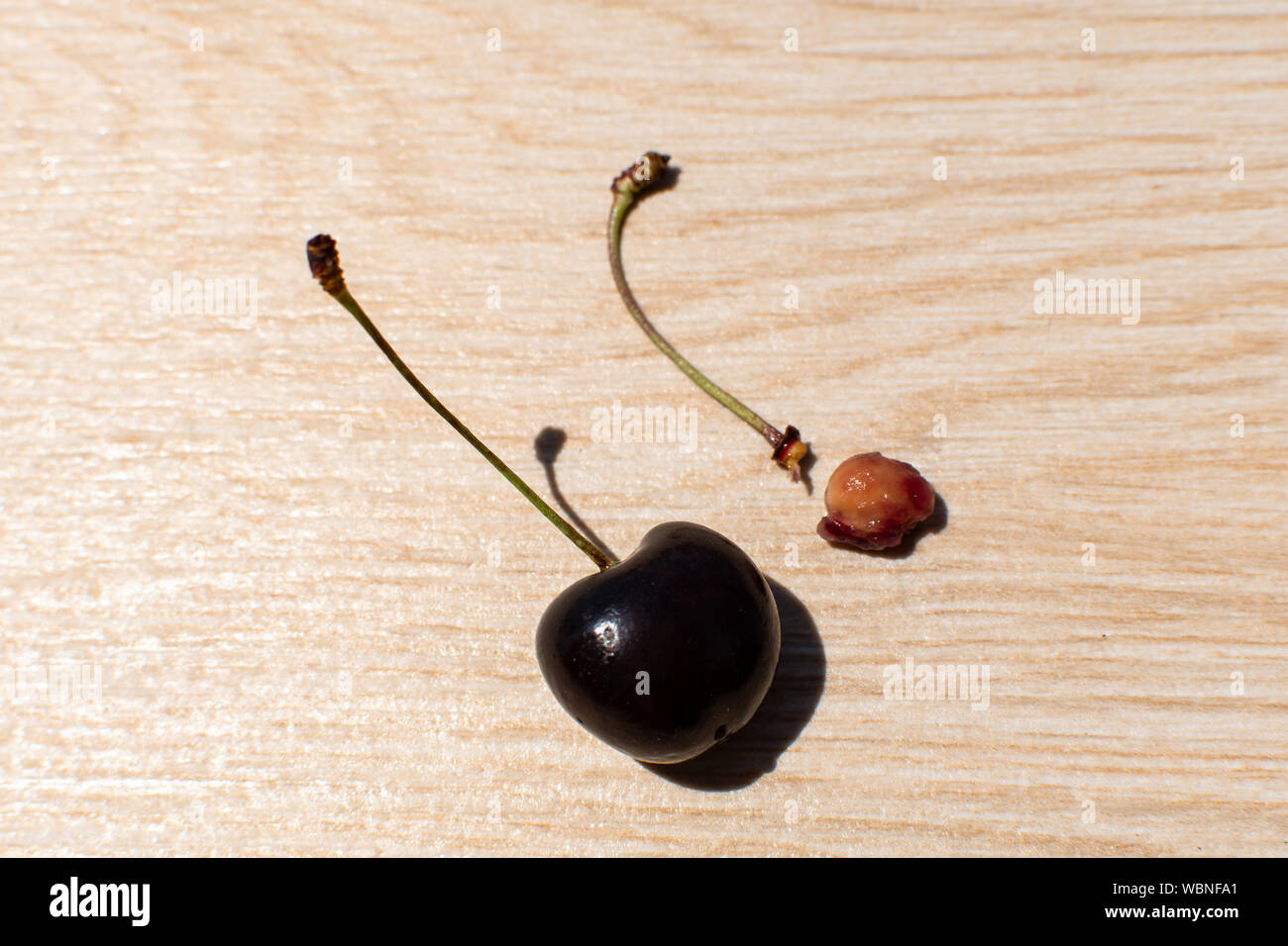 Eine normale rote Bing cherry Neben einem Stamm eines gegessen cherry Früchte. Auf hölzernen Hintergrund. Kopieren Sie Platz. Stockfoto