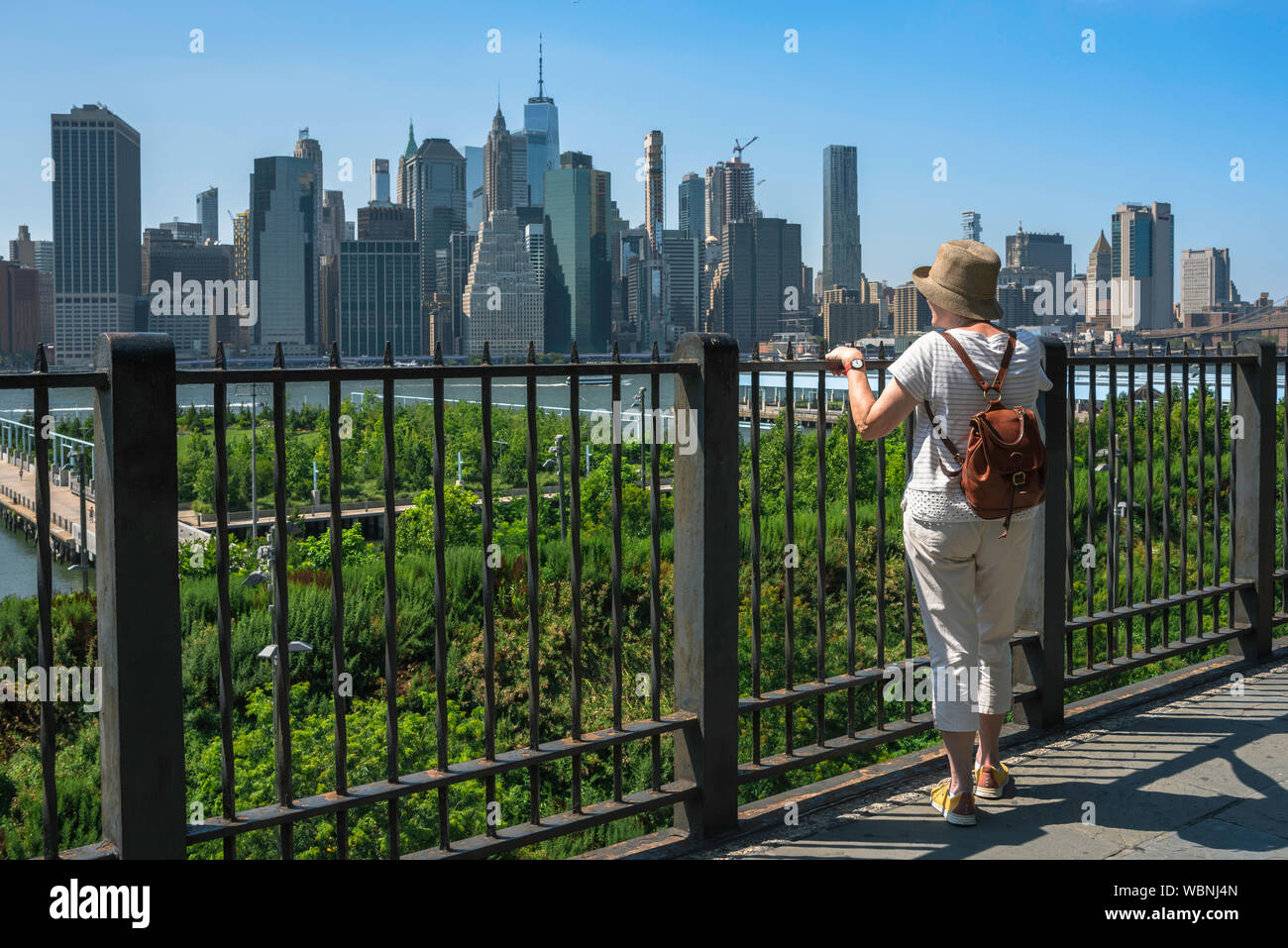 Reife Frau Stadt, Ansicht der Rückseite einer reifen Frau, die auf der Promenade in Brooklyn im Sommer und mit Blick auf die Skyline von Manhattan, New York City, USA Stockfoto