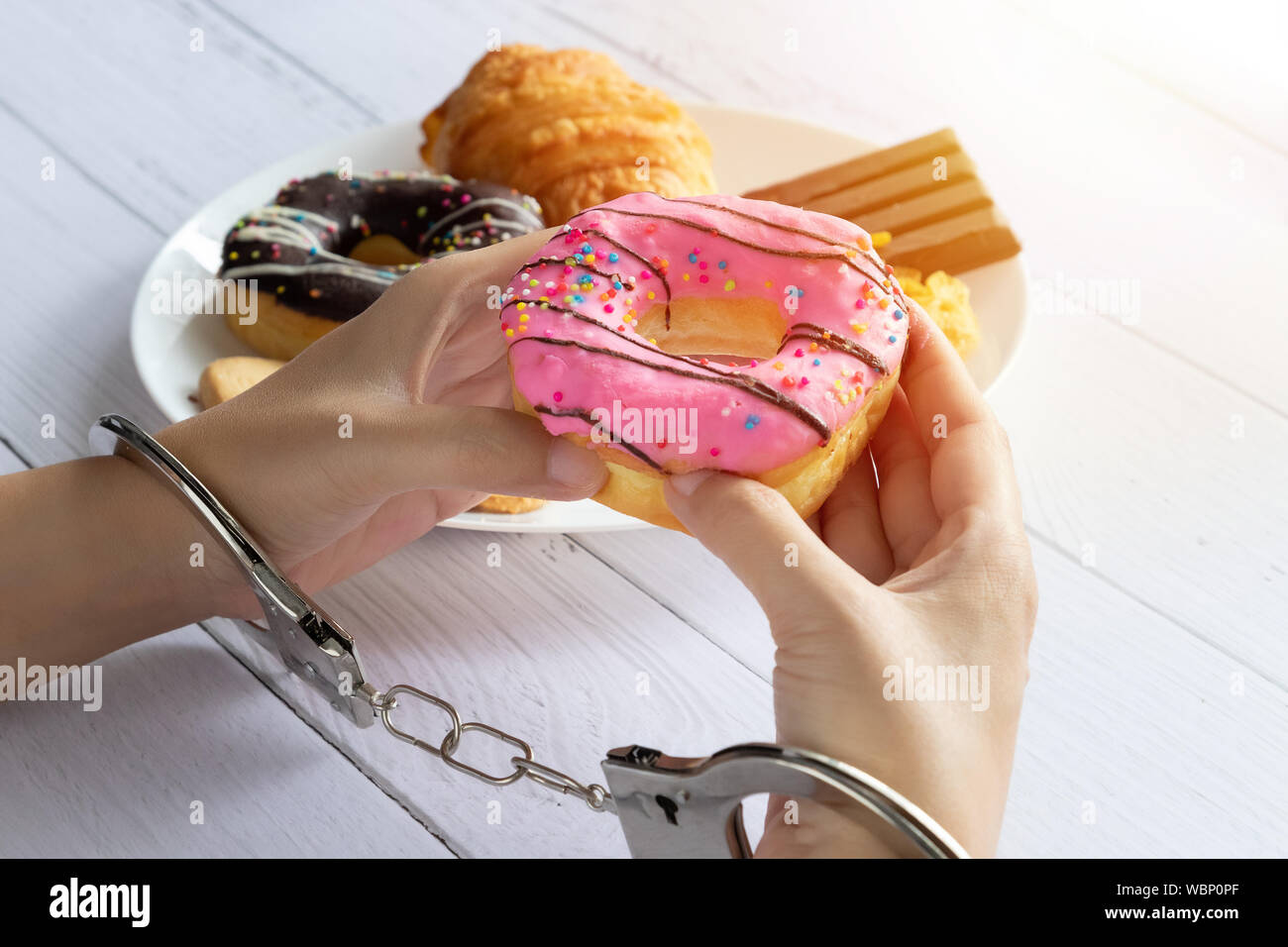 Kalorien, Ernährung und Gewichtsabnahme Konzept. nach oben Blick auf zwei Händen war Kontrolle durch Handschellen, holding Donut aus weißen Teller auf Esstisch Stockfoto