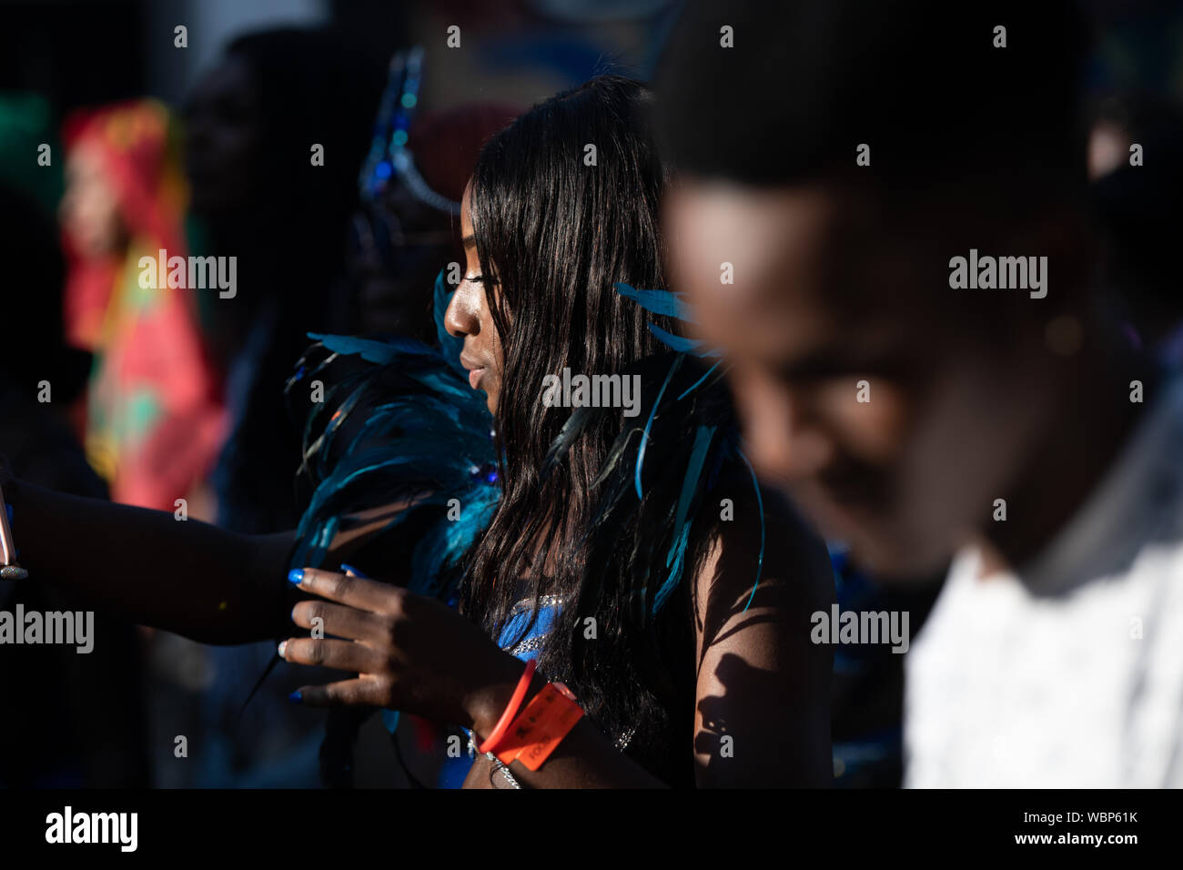 Eine schwarze Frau in einer Masse an der Notting Hill Carnival durch blaue Federn umgeben. Stockfoto
