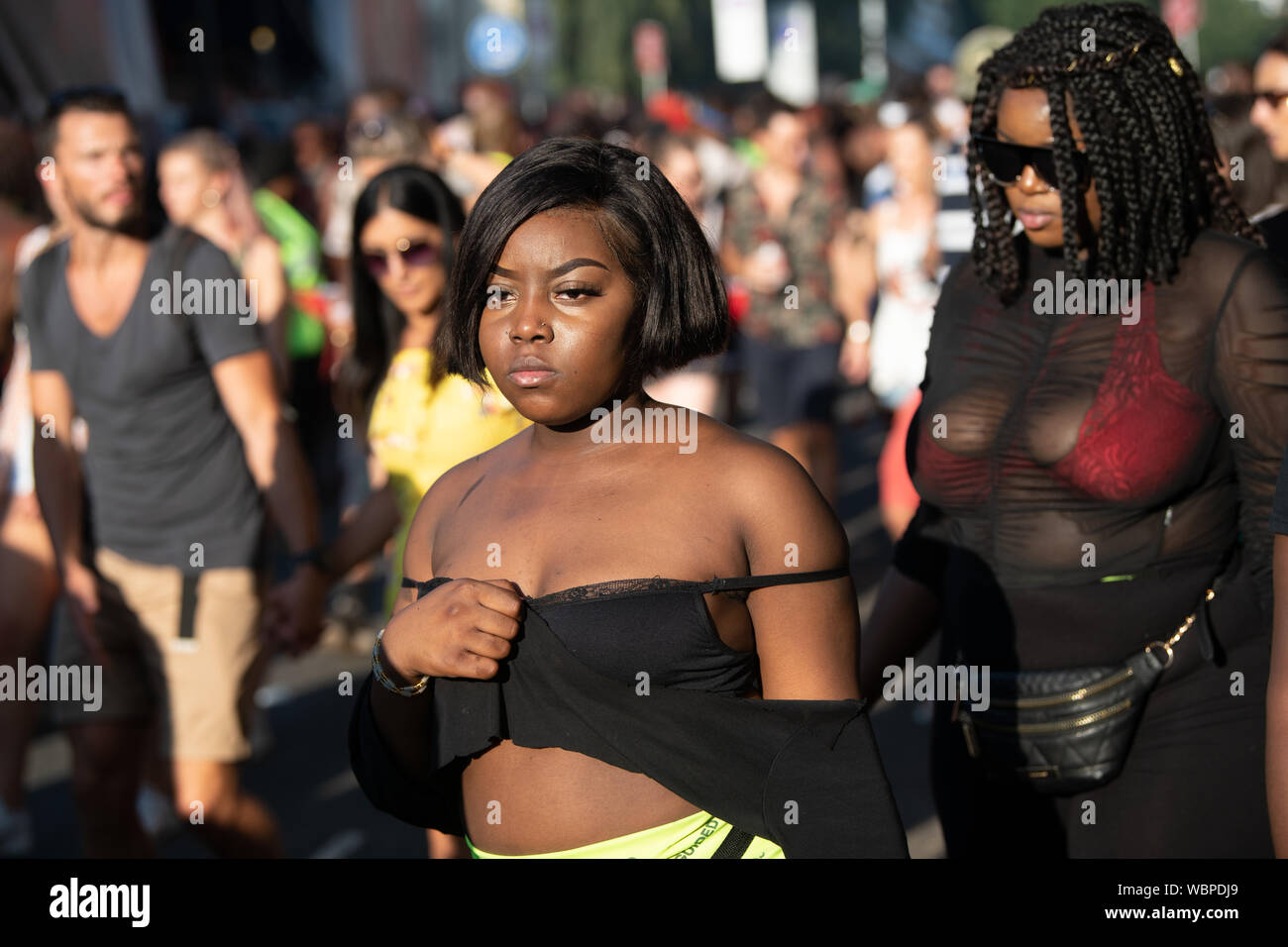 Eine junge schwarze Frau mit schwarzen steht in der Mitte von einer Masse an der Notting Hill Carnival. Stockfoto