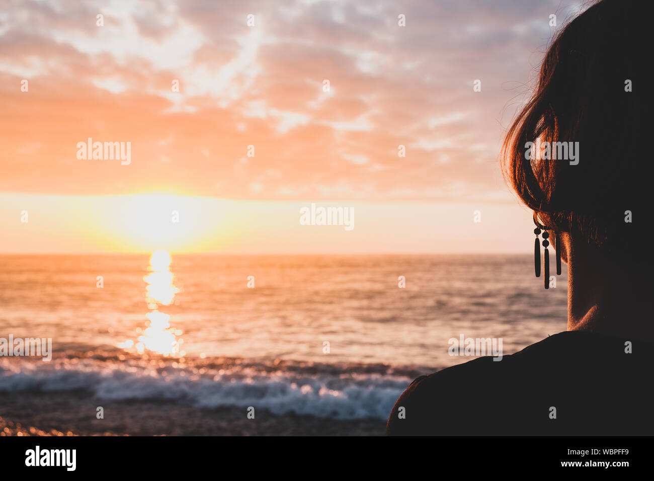 Genießen Sie das Meer auf einem felsigen Strand, geschossen von hinter der Person. Weibliche Person sitzt in den Sonnenuntergang der Sonnenuntergang Stockfoto