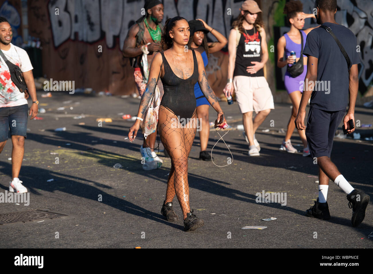 Eine Frau in einem schwarzen bodysuit und Netzstrumpfhose zu Fuß durch eine Straße auf Karneval ihr Telefon Holding. Stockfoto