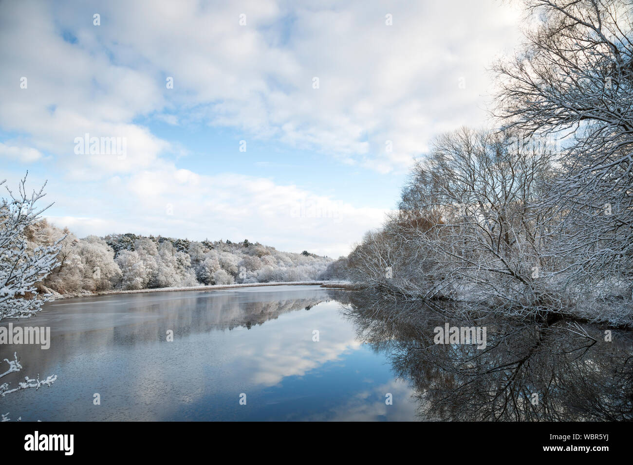 Winterlandschaft in Großbritannien nach Schneefall. Blick auf den britischen See an einem sonnigen Morgen in der Wintersaison mit Schnee auf Bäumen. Stockfoto