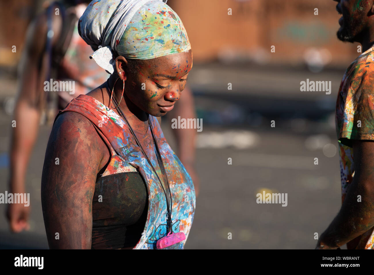 Eine schwarze Frau in Notting Hill Carnival erhalten in der Farbe bedeckt und lächelnd. Stockfoto