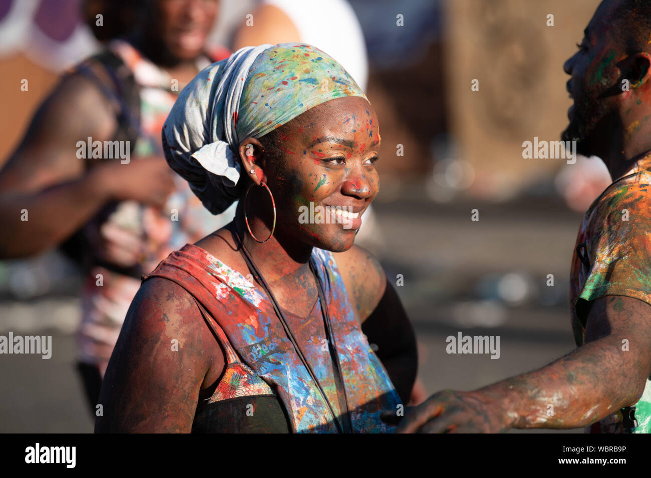 Eine schwarze Frau in Notting Hill Carnival erhalten in der Farbe bedeckt und lächelnd. Stockfoto