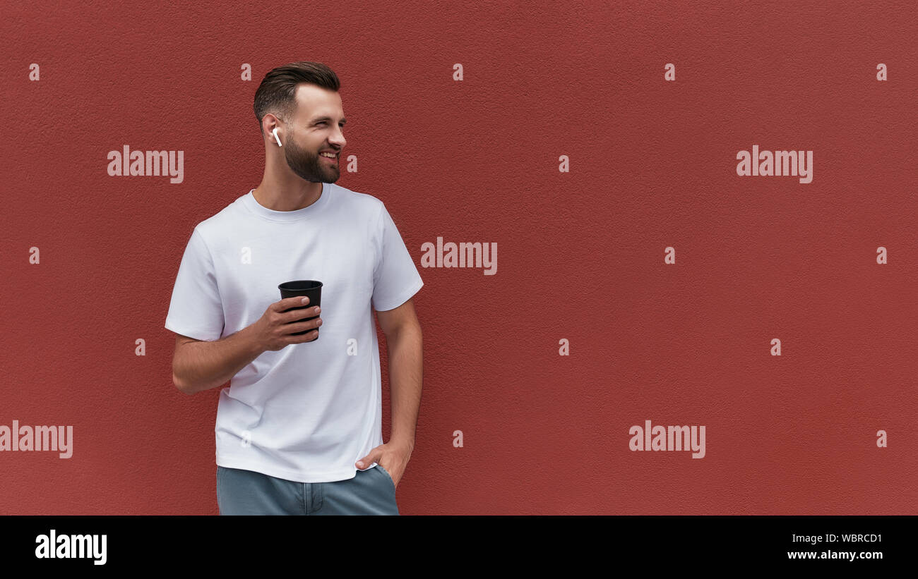 Ich liebe meine Stadt. Stattlich und fröhlichen Menschen in Freizeitkleidung holding Tasse Kaffee und beiseite mit Lächeln, während gegen die Rote Wand im Freien stehen. Web Banner Stockfoto