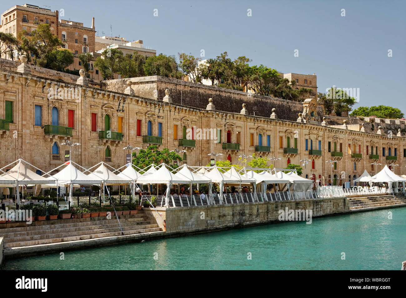 Waterfront; alte Kalkstein Bauwerke und bunten Fensterläden; Grün; Weiß sonnenschirme Balkon Geländer; Wiederholung; Muster, Tische, Stühle, im Freien zu essen, Stockfoto