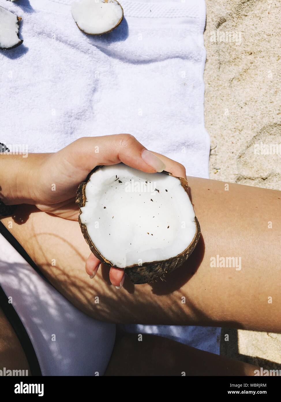 Mittelteil der Frau mit Kokosnussschalen am Strand Während der sonnigen Tag Stockfoto