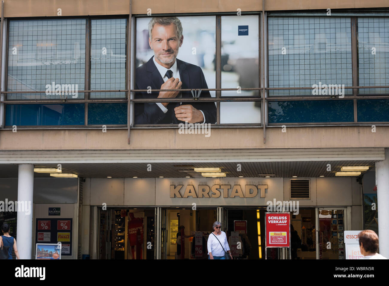 Frau verlassen einer Karstadt Fashion Store mit einem Poster von einem perfekt gekleideter Mann in Mainz, Deutschland Stockfoto