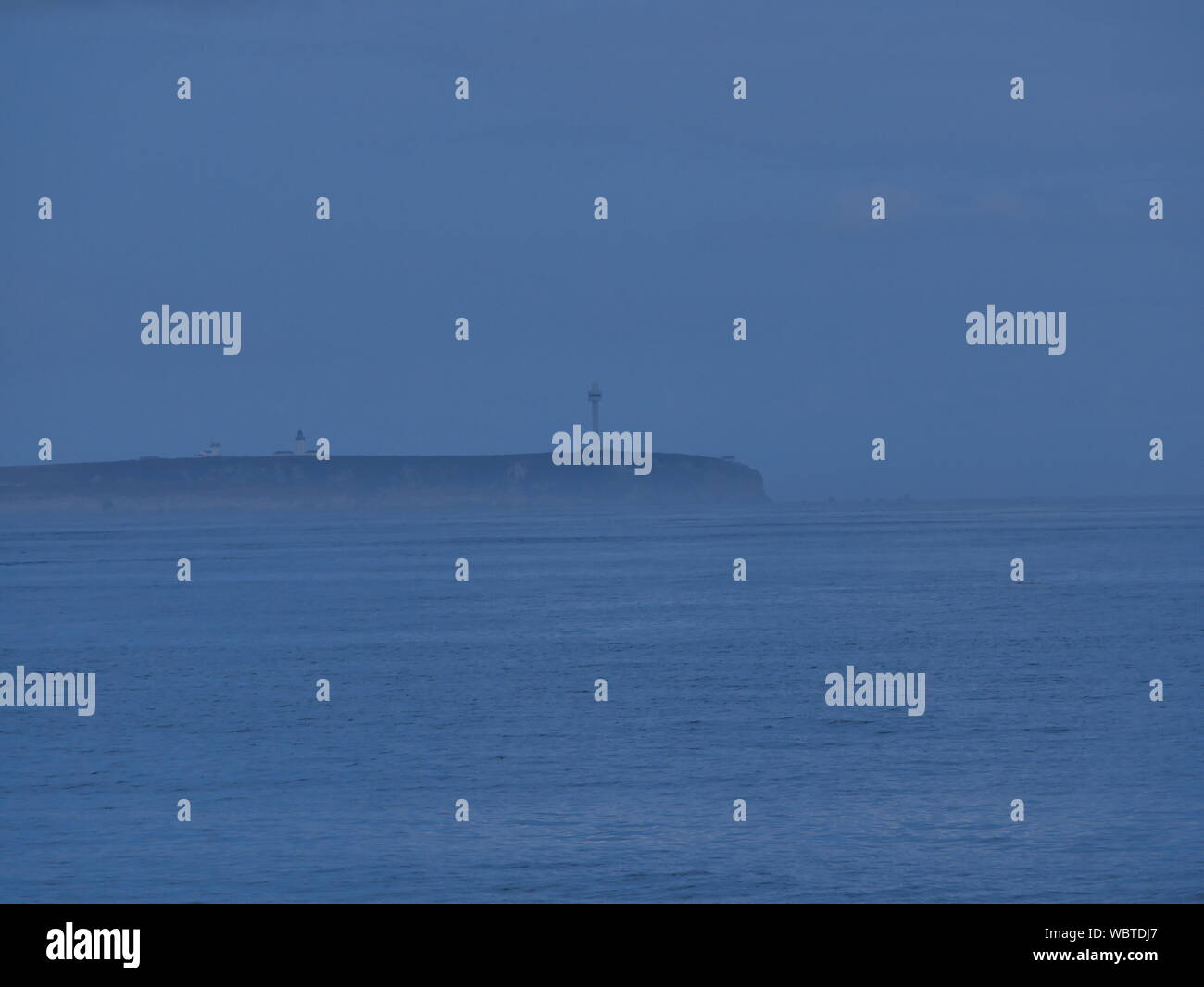 Foto de l'île de Ouessant dans la brume avec une mer calme avec au bout de l'île, la tour Radar de Ouessant et ses abruptes falaises. Stockfoto