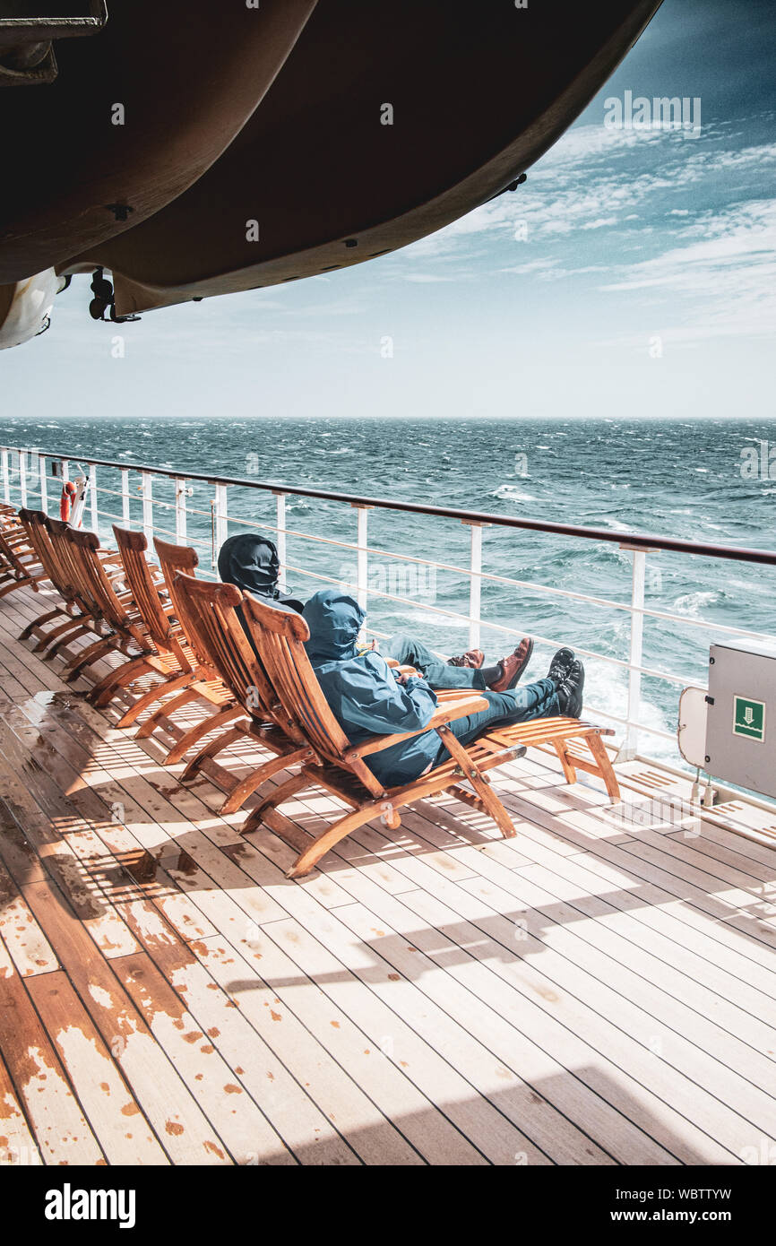 Passagier bis gegen die Aussteifung Nordsee gewickelt auf dem Deck der Cunard Ocean Liner und flagship Schiff, der Queen Mary 2 Gale, als sie in Großbritannien Segel Stockfoto