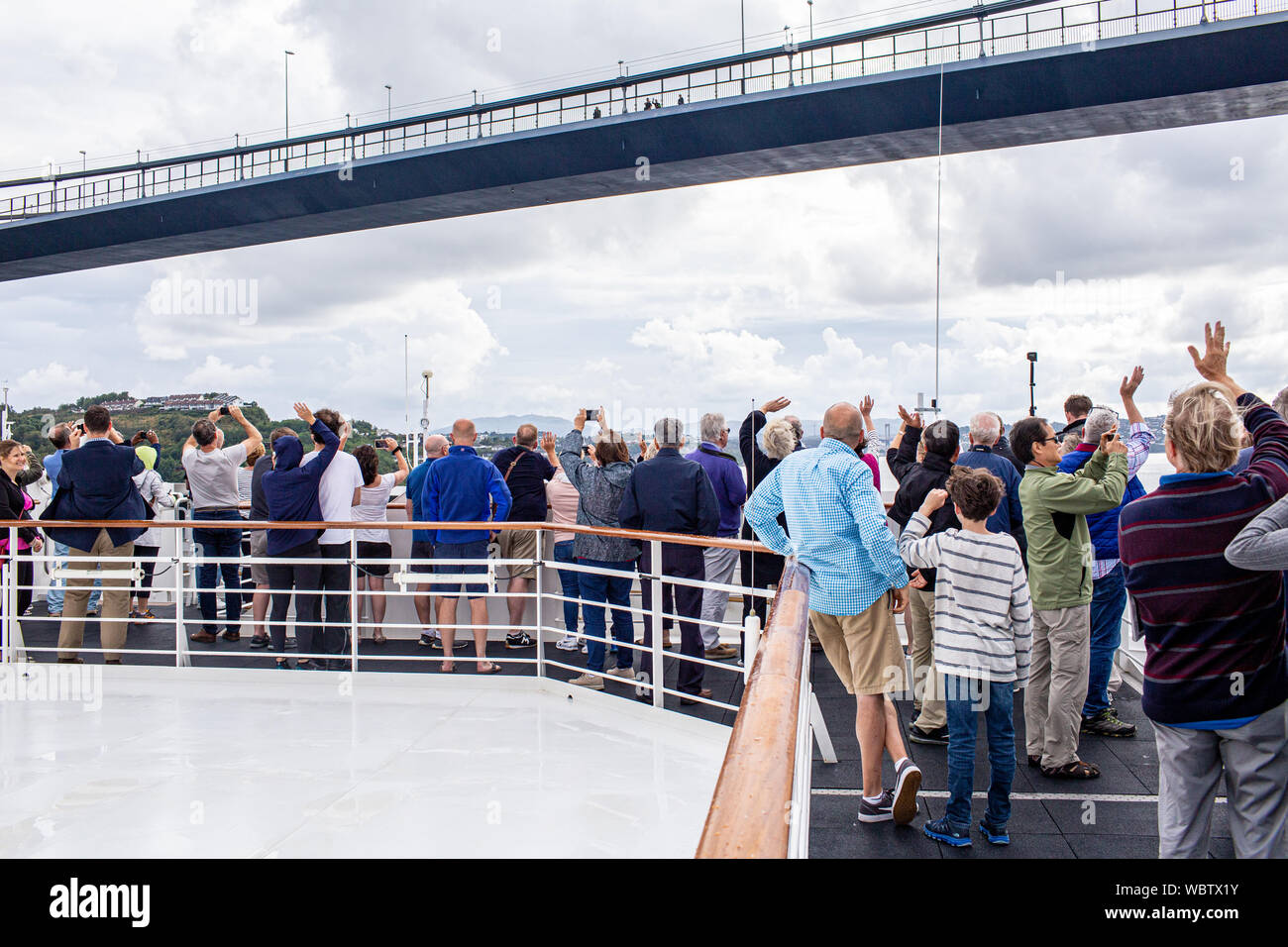 Gruppe der Kreuzfahrtpassagiere wave für Pendler auf einem Bergen Brücke, da sie sehr nahe an der Unterseite der Struktur segeln. Stockfoto