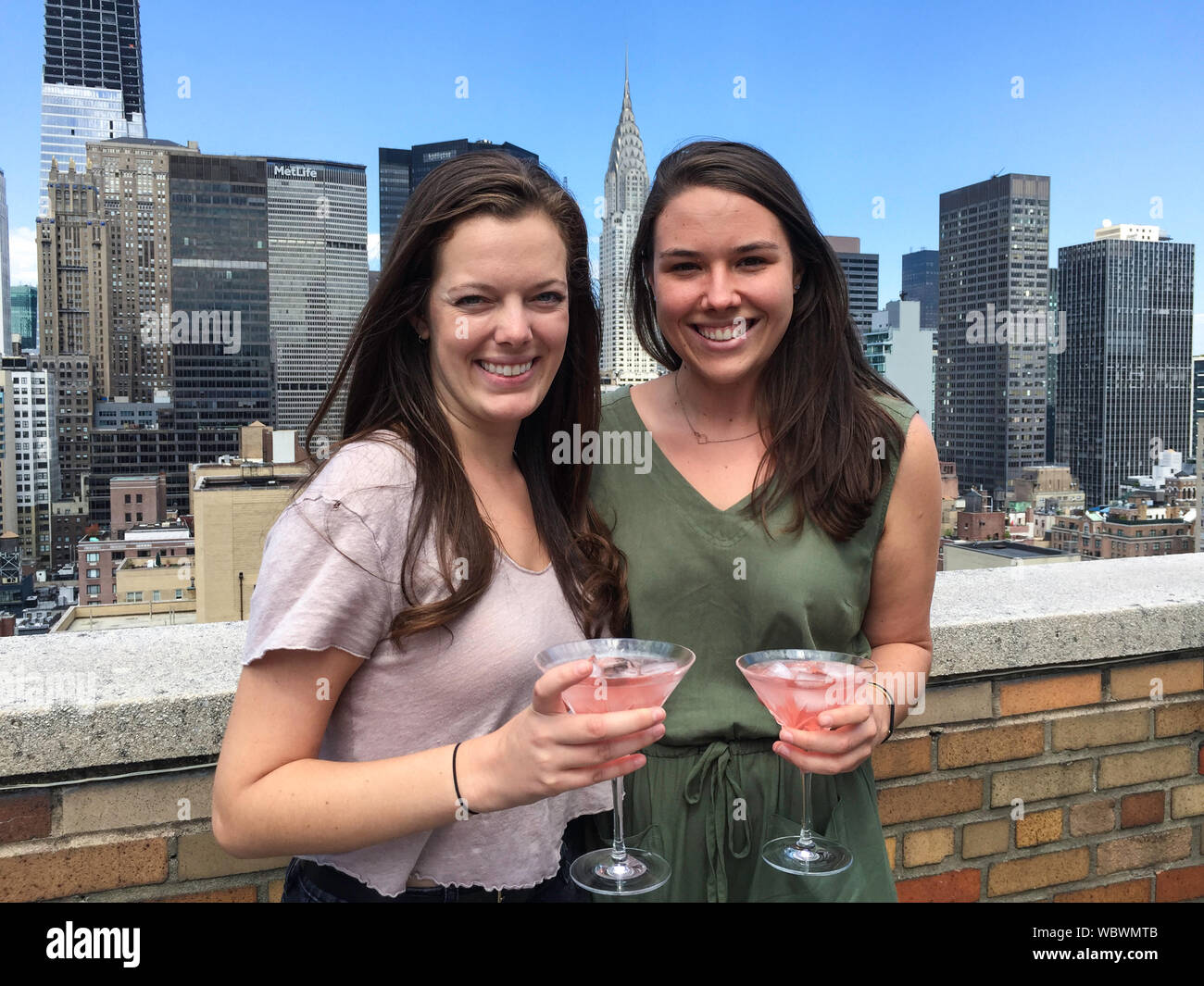 Zwei College-Freunde aus der Mitte der Zwanziger Jahre genießen einen Cosmopolitan auf einem Dachdeck des Apartmenthauses in Murray Hill, NYC, USA Stockfoto