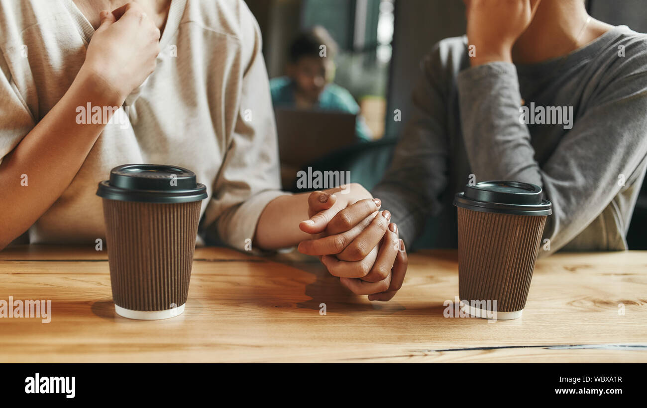 7/8-Porträt von zwei jungen Frauen, die sich in einander die Hände, wie sie in der Cafeteria genießen eine Tasse Kaffee sitzen. Horizontale erschossen. Ansicht von vorn Stockfoto