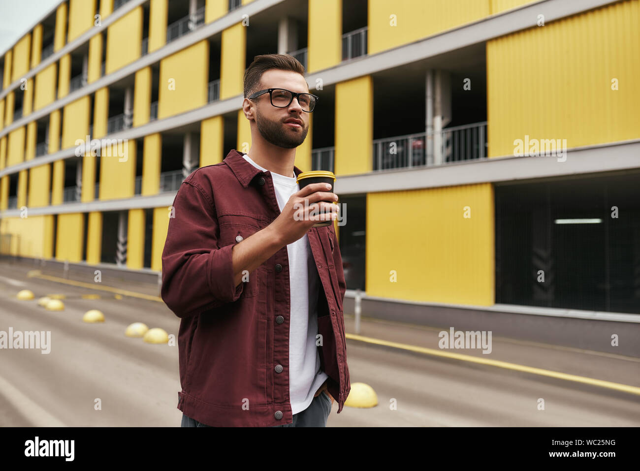Großer Tag. Hübscher junger Mann in Freizeitkleidung und bärtigen Mann in Brillen mit einer Wegwerf-cup beim Bummel durch die Stadt. Urban Style Stockfoto