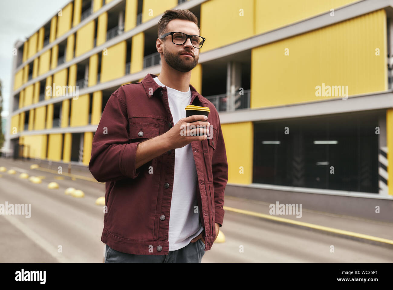 Ich liebe meine Stadt. Hübscher junger bärtiger Mann in Freizeitkleidung und Brillen mit einer Wegwerf-cup beim Bummel durch die Stadt. Urban Style Stockfoto