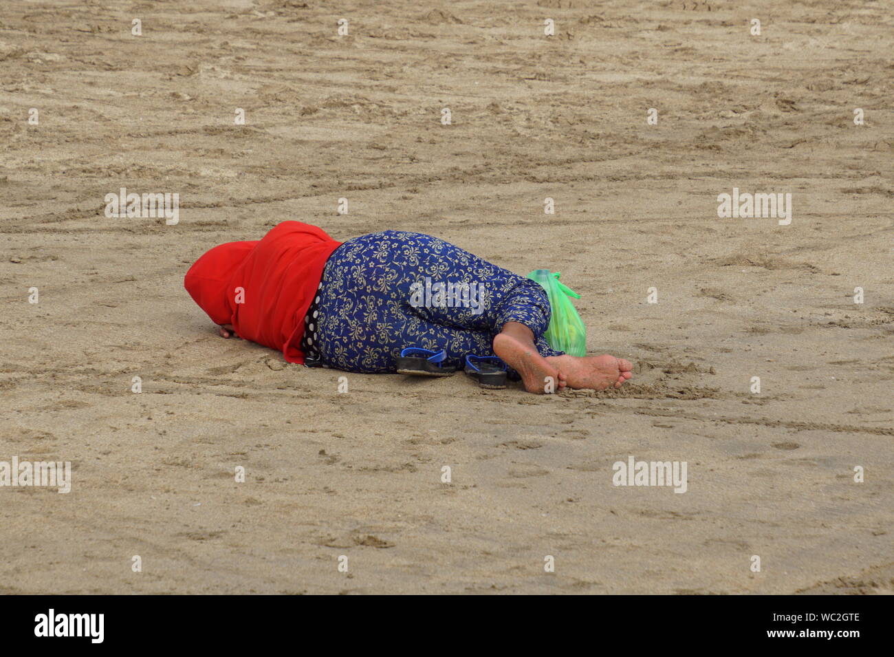 Unbekannte und nicht identifizierbare obdachlose Frau liegen auf einem Strand. Stockfoto