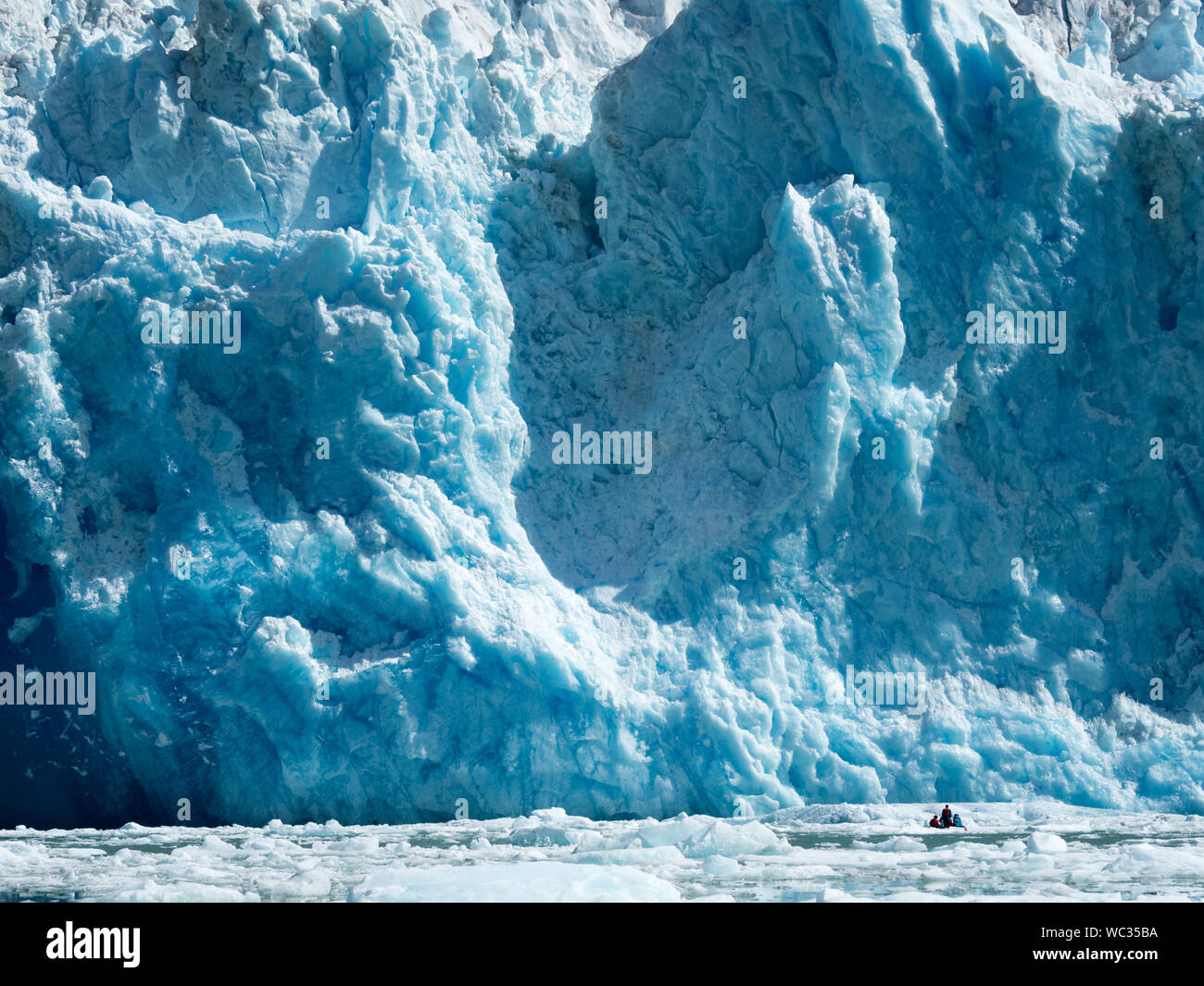 Ökotouristen in einem kleinen Boot beobachten eine massive Kalbungsveranstaltung auf dem South Sawyer Glacier in Tracy Arm, Südost-Alaska, USA Stockfoto