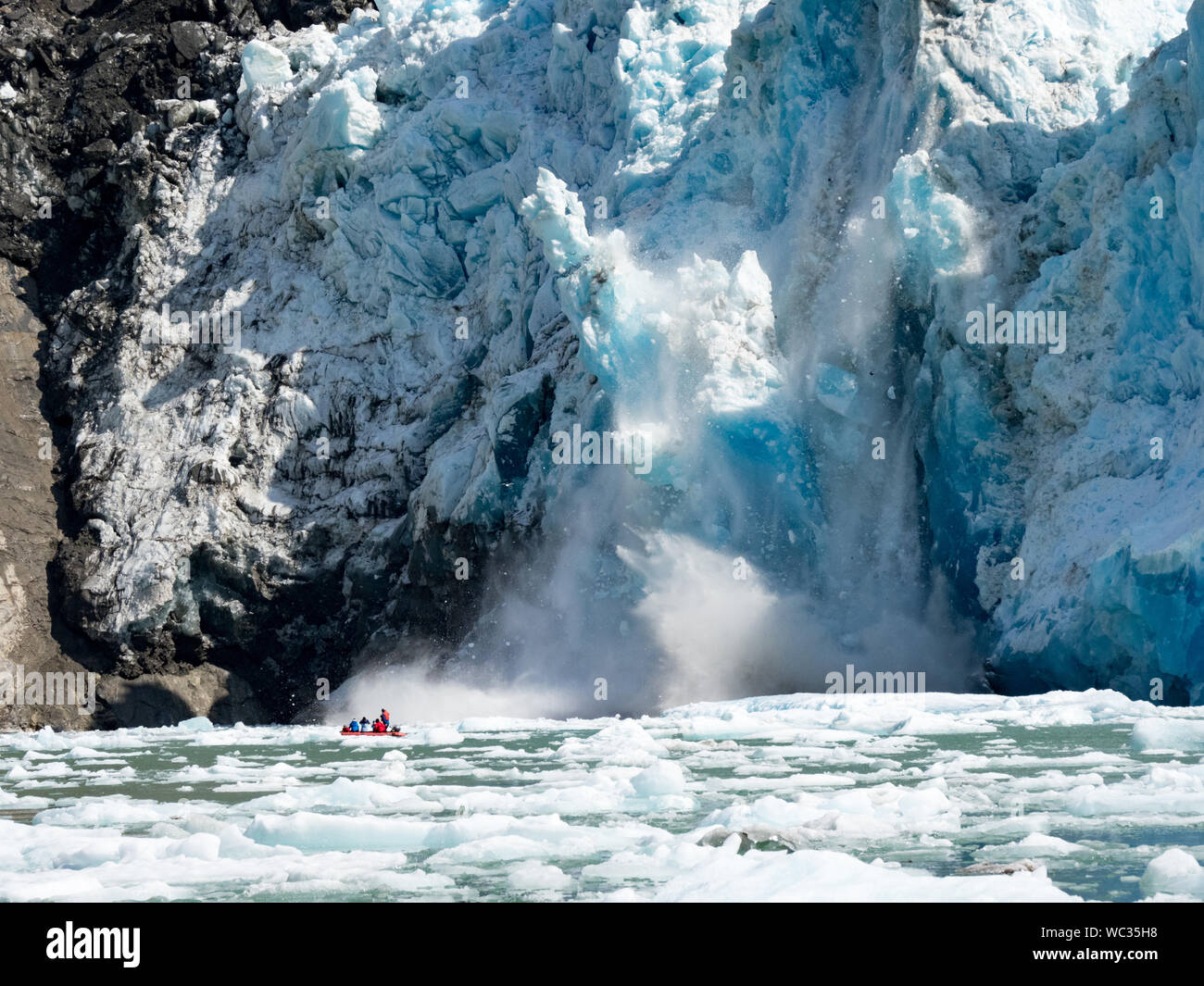 Ökotouristen in einem kleinen Boot beobachten eine massive Kalbungsveranstaltung auf dem South Sawyer Glacier in Tracy Arm, Südost-Alaska, USA Stockfoto