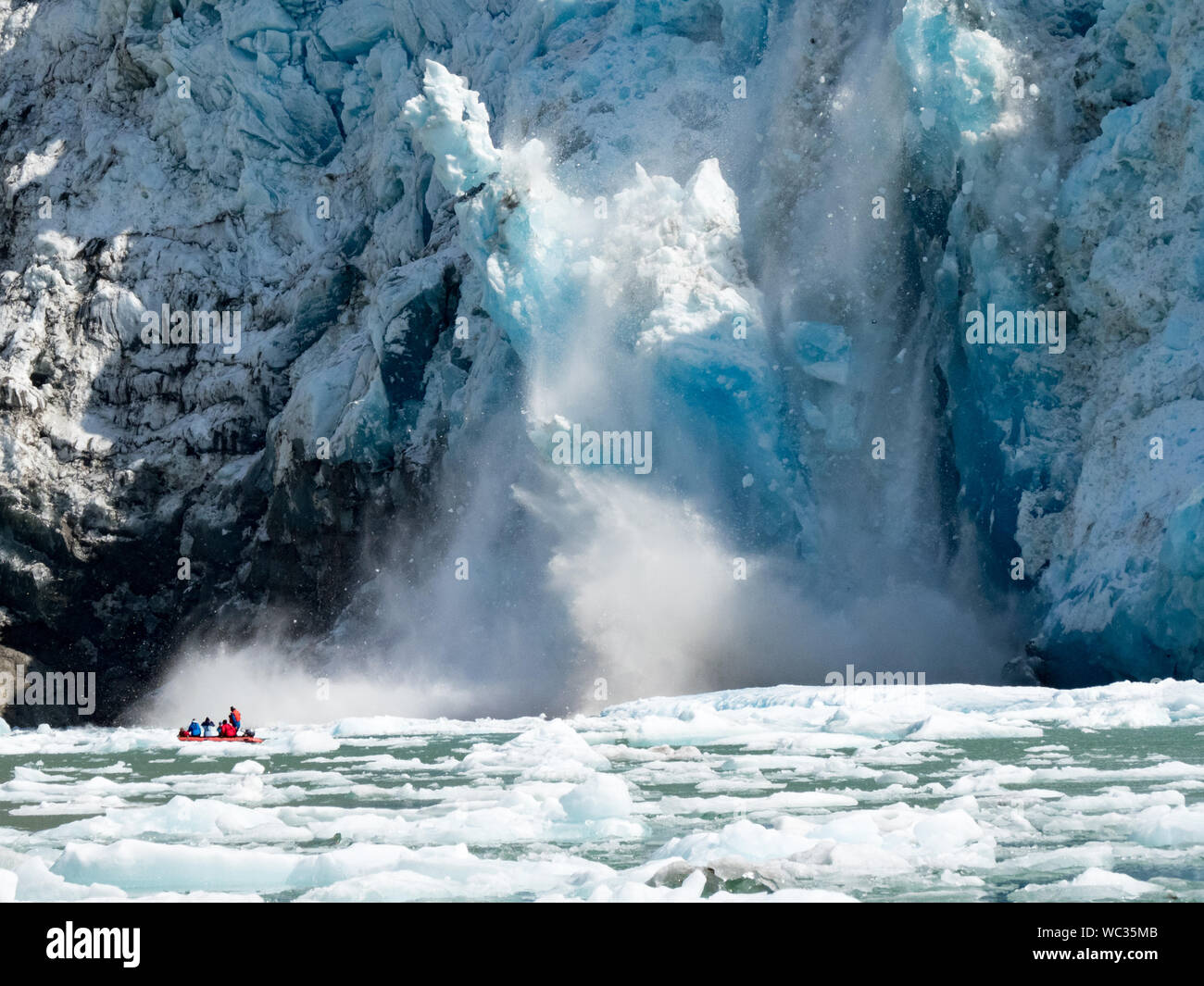 Ökotouristen in einem kleinen Boot beobachten eine massive Kalbungsveranstaltung auf dem South Sawyer Glacier in Tracy Arm, Südost-Alaska, USA Stockfoto