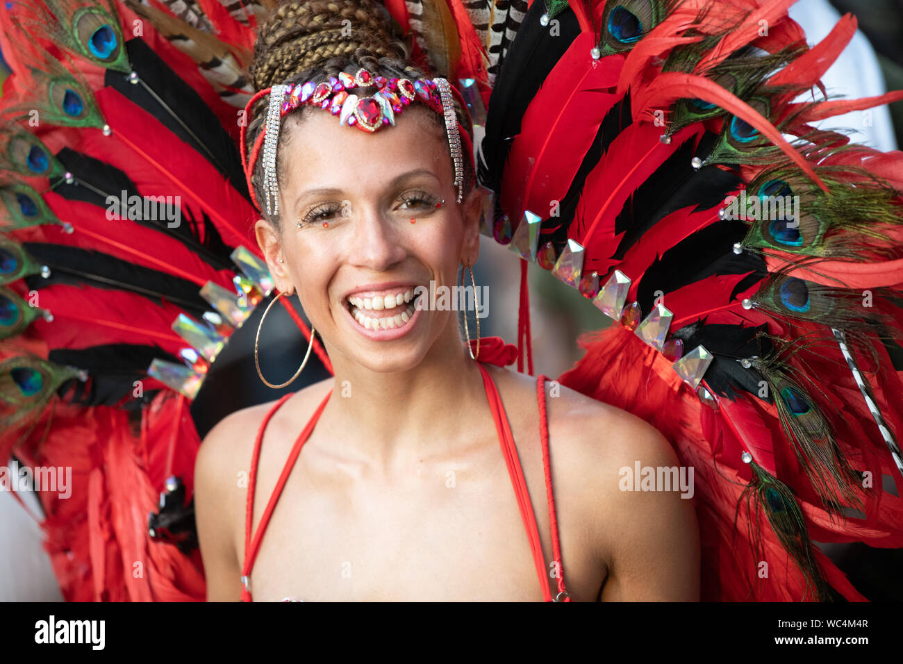 Performerin gekleidet in bunte Federn in die Kamera bei der Notting Hill Carnival, größte Karneval in Europa suchen. Stockfoto