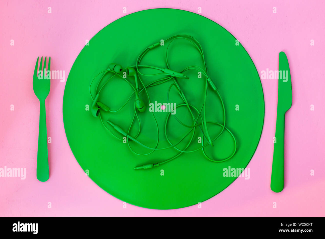 Kreatives Konzept aufnehmen Teller mit Messer, Gabel, Kopfhörer auf einem rosa Hintergrund Stockfoto