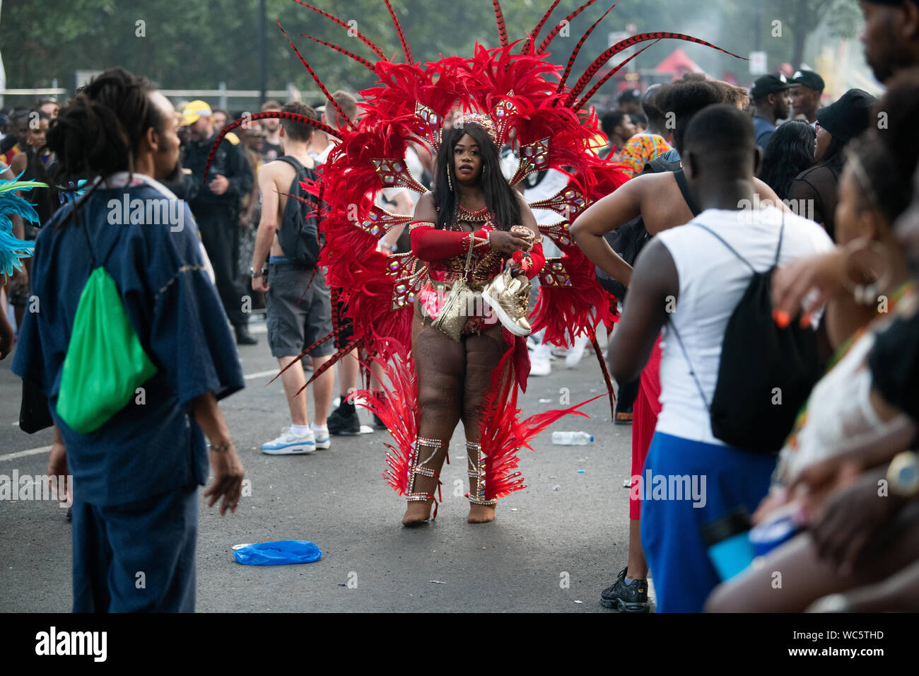 Eine Frau von Rot und Orange federn sie an einer Parade in Notting Hill Carnival umgeben, gekleidet in Tracht. Stockfoto
