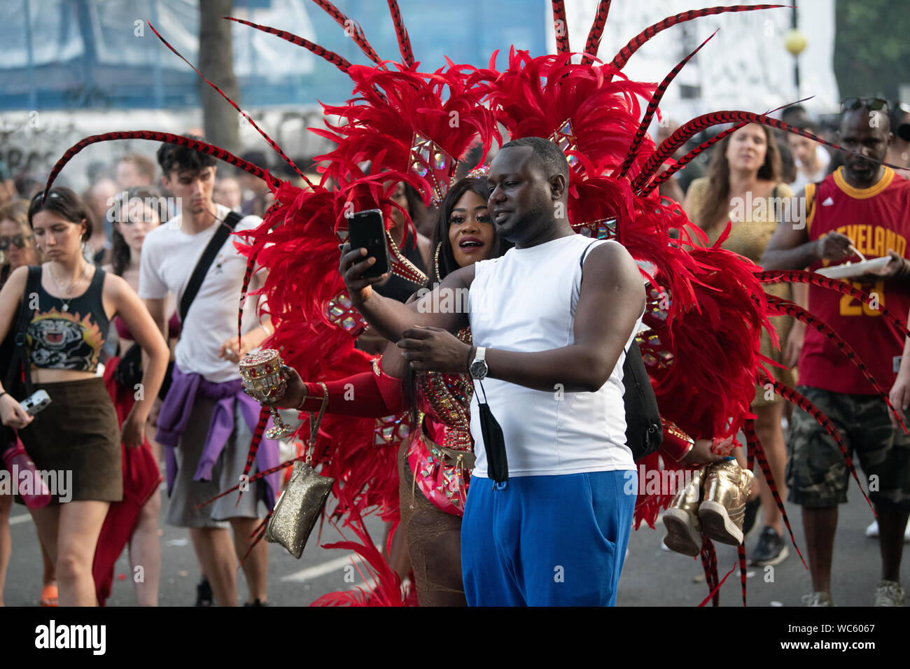 Ein Mann mit einem selfie mit einer Frau in der Notting Hill Carnival Gekleidet in rote Federn. Stockfoto