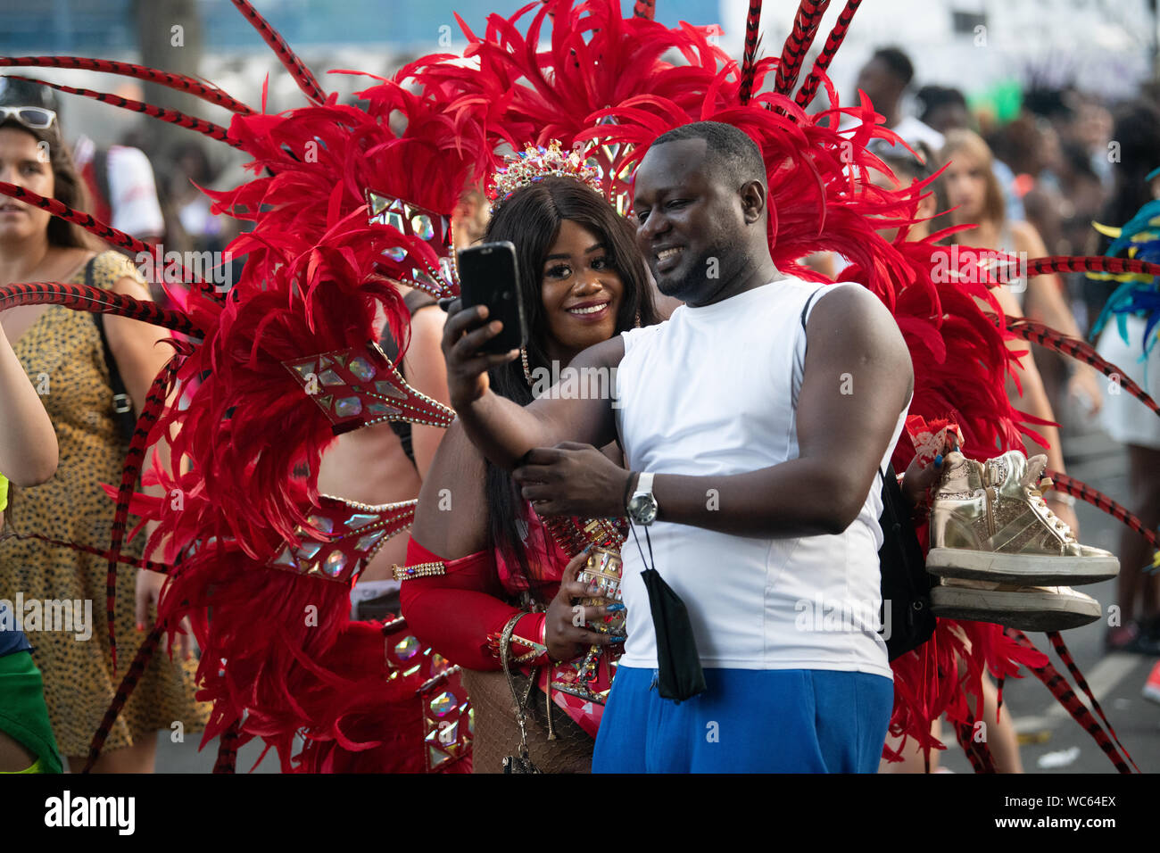 Ein Mann mit einem selfie mit einer Frau in der Notting Hill Carnival Gekleidet in rote Federn. Stockfoto