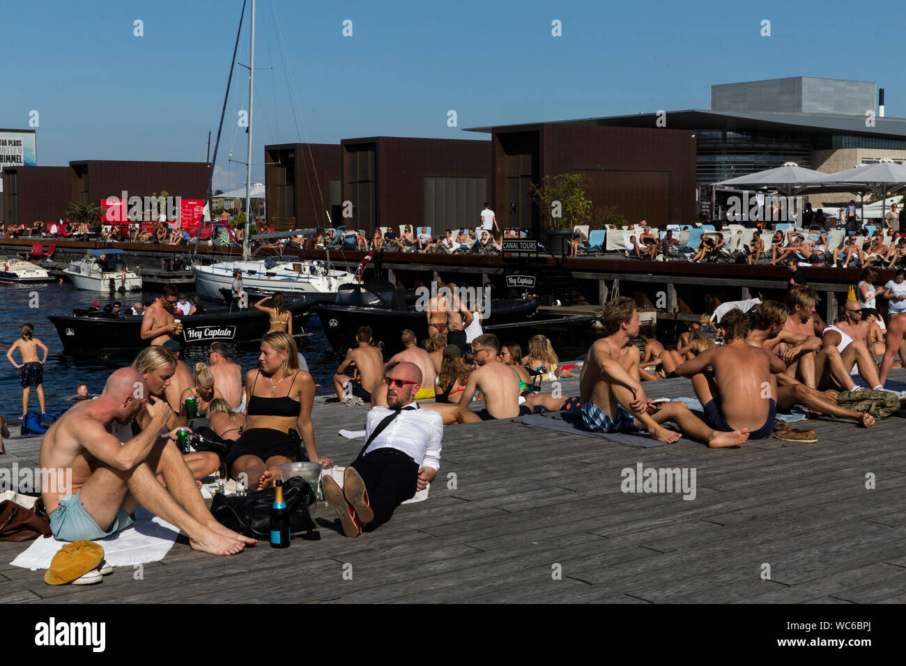 Kopenhagener und Touristen an der hölzernen Pier in Ofelia Platz in der Nähe des Royal Play House (R) und die historische Nyhavn in Kopenhagen, Dänemark. Das Wasser in den Hafen von Kopenhagen ist so sauber, dass es sicher ist, ein erfrischendes Bad zu nehmen. Im Jahr 2018 überstieg in Kopenhagen der CNN-Liste für "besten Städte für Schwimmen". Stockfoto