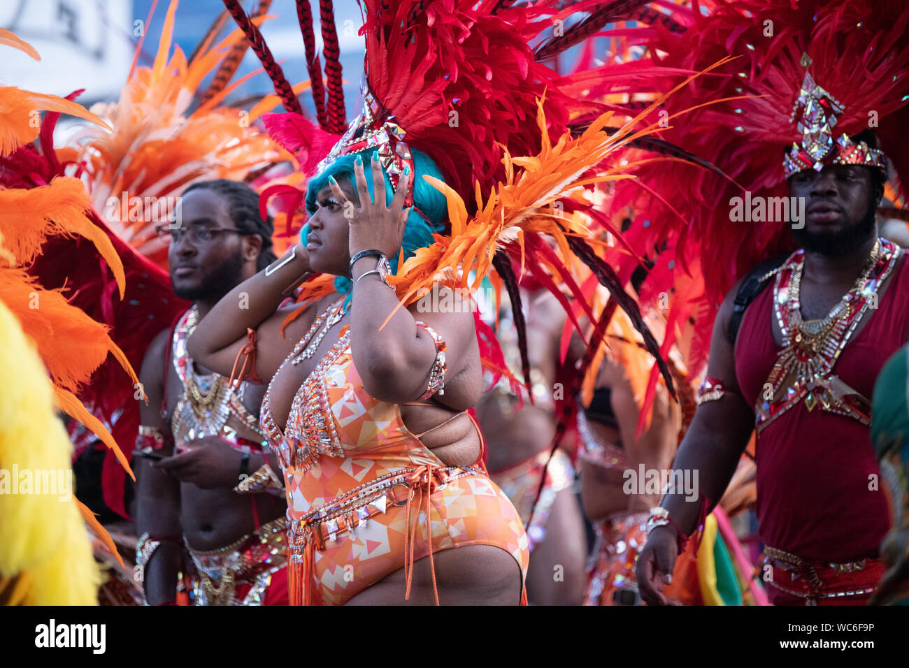Eine Frau von Rot und Orange federn sie an einer Parade in Notting Hill Carnival umgeben, gekleidet in Tracht. Stockfoto
