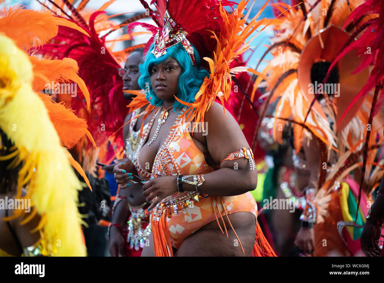 Eine Frau von Rot und Orange federn sie an einer Parade in Notting Hill Carnival umgeben, gekleidet in Tracht. Stockfoto