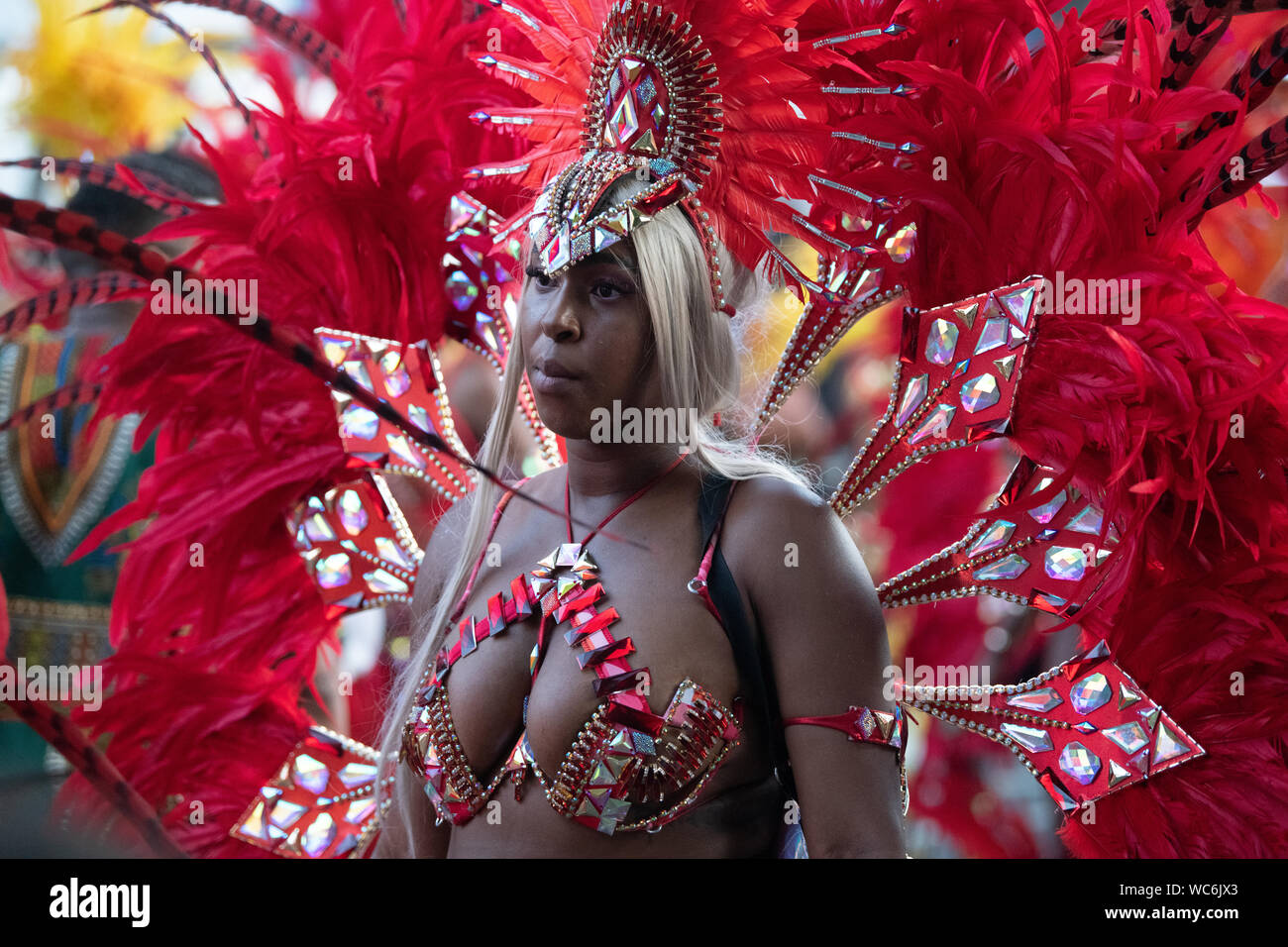 Eine Frau von Rot und Orange federn sie an einer Parade in Notting Hill Carnival umgeben, gekleidet in Tracht. Stockfoto