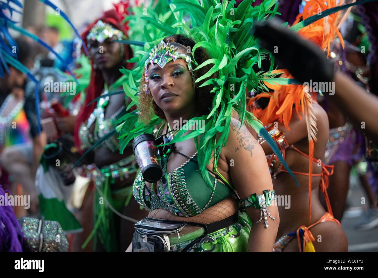 Tänzerin Federn tragen und sich mit der Kamera an der Notting Hill Carnival in London, der größten Straße Karneval in Europa Stockfoto