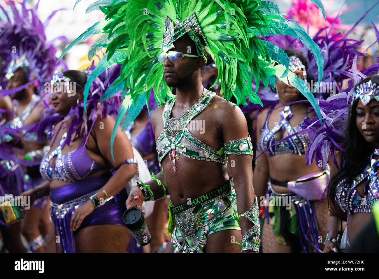 Männliche Tänzer Federn tragen und Blick in die Kamera bei der Notting Hill Carnival in London. Andere Tänzer im Hintergrund Stockfoto