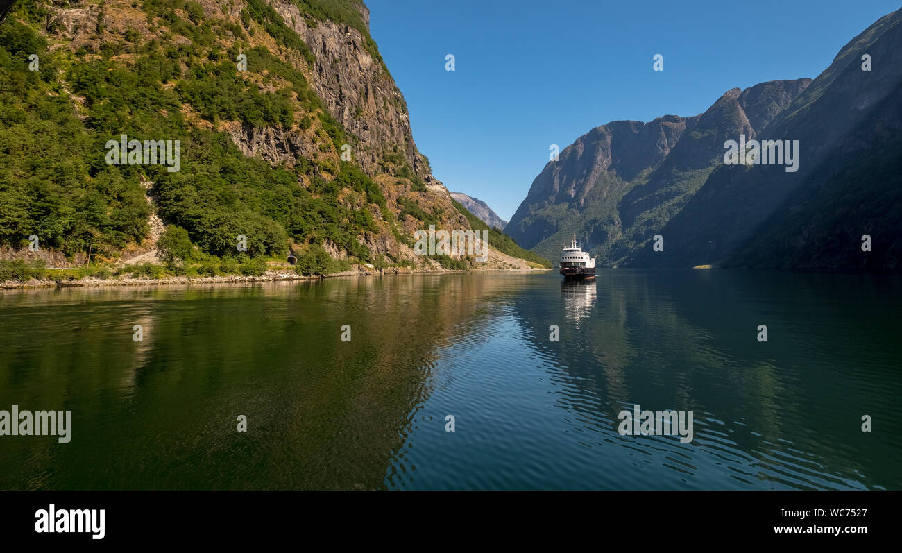 Ein sich näherndes Ausflug Schiff auf einer wunderschönen Fjord, wo das Licht reflektiert, von Felsen teilweise bedeckt mit Bäumen umgeben, mit einem strahlend blauen Himmel Stockfoto