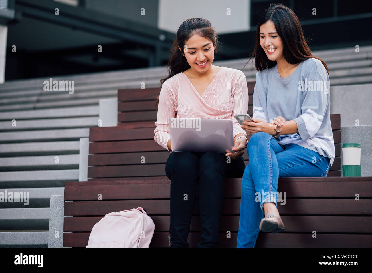 Smart lächelnd Asiatische Frauen studieren an Notebook sprechen und Sitzen in hölzerne Treppe Stockfoto