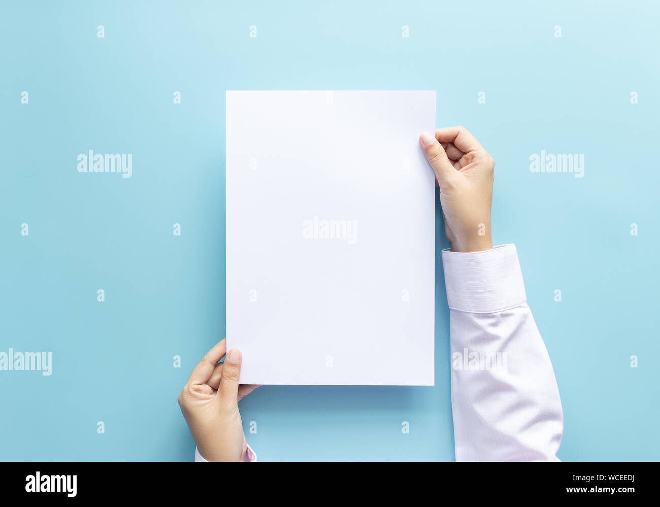 Die Hände schließen Holding leere weiße Leere schreiben Papierformat A4 für Flyer oder Einladung mock up auf einem blauen Hintergrund. Stockfoto