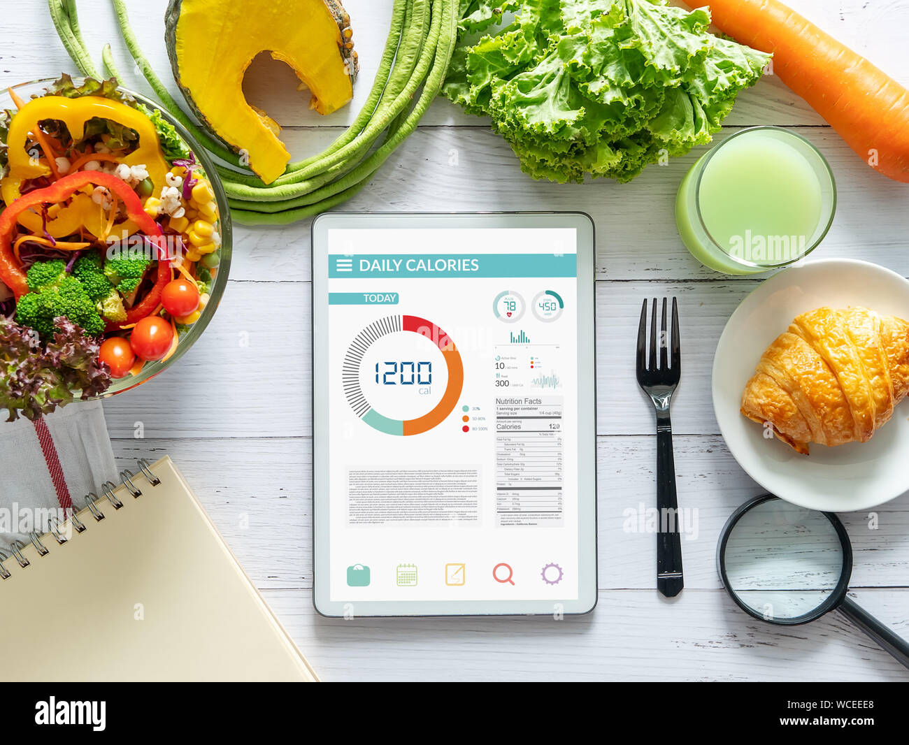 Kalorien zählen, Ernährung, der Kontrolle und Gewichtsverlust Konzept. Tablet mit Kalorienzähler Anwendung auf dem Bildschirm am Esstisch mit Salat, Obst j Stockfoto