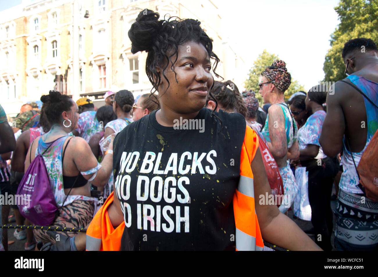 Notting Hill Carnival, 25. August 2019. Eine schwarze Frau trägt ein T-Shirt mit der Aufschrift "Keine schwarzen, keine Hunde, für die es keine irischen', die sich auf Mitteilungen Werbung Zimmer Stockfoto