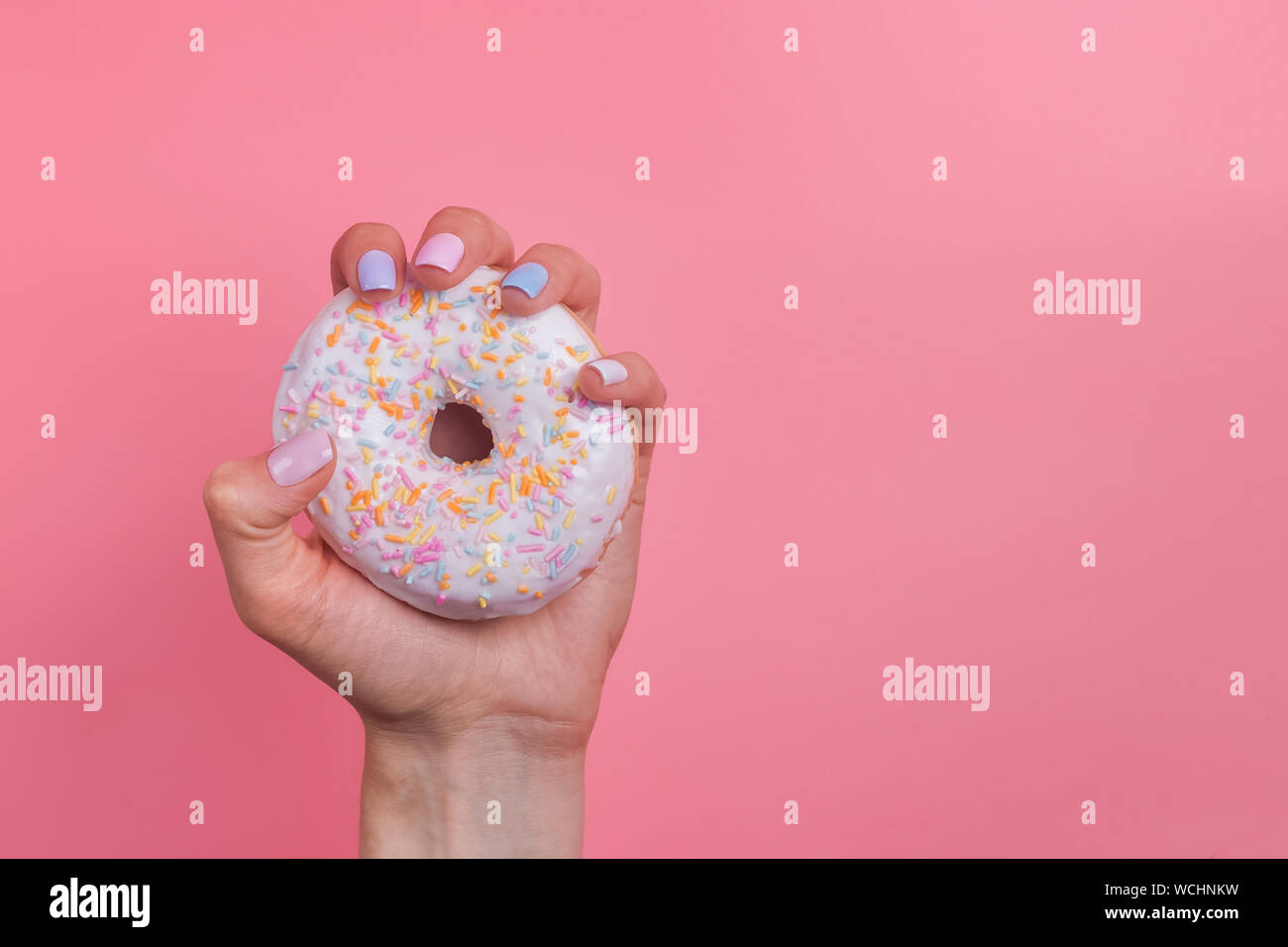 Woman's Hand mit Maniküre Holding einen Krapfen auf rosa Hintergrund Stockfoto