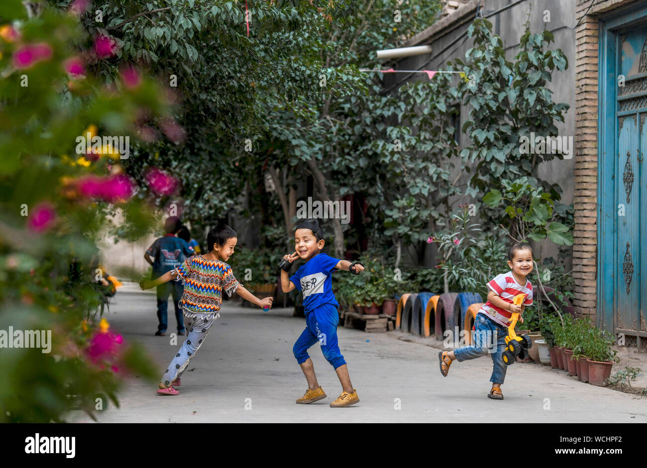(190828) - KASHGAR, Aug 28, 2019 (Xinhua) - Kinder haben Spaß in einer Gasse im Dorf Qianjin in Kashgar, Nordwesten Chinas Autonome Region Xinjiang Uygur, Aug 18., 2019. Wohnungen von duftenden Blüten im Überfluss umgeben, übersichtliche Häuser und Gassen von einem gepflegten Erscheinungsbild, verschiedene Bäume entlang der Straßen, wo die Kinder sich genießen, die pastorale Szene überall in Qianjin Dorf gesehen werden kann. Die idyllische Schönheit in Qianjin Dorf leitet sich aus seiner boomenden Wirtschaft, in der Blume Salima Sultan ist ein Pionier. Salima, ein 60-jähriger Dorfbewohner, entwickelte sich die Vorliebe der f Stockfoto