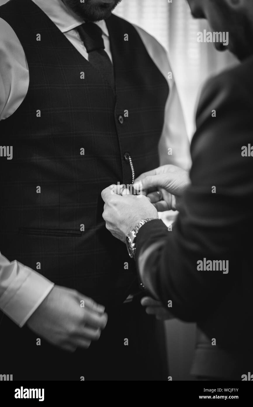 Vertikale Graustufenaufnahme eines Mannes, der die Jacke seines Freundes knöpfte Für die Hochzeit Stockfoto