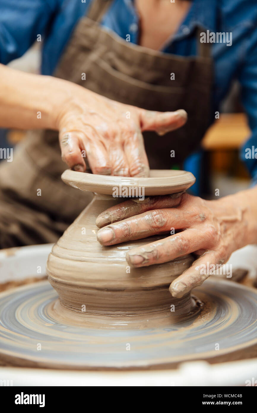 Hände von älteren weiblichen Potter arbeiten an Töpferei Rad beim Sitzen in ihrem Workshop Stockfoto