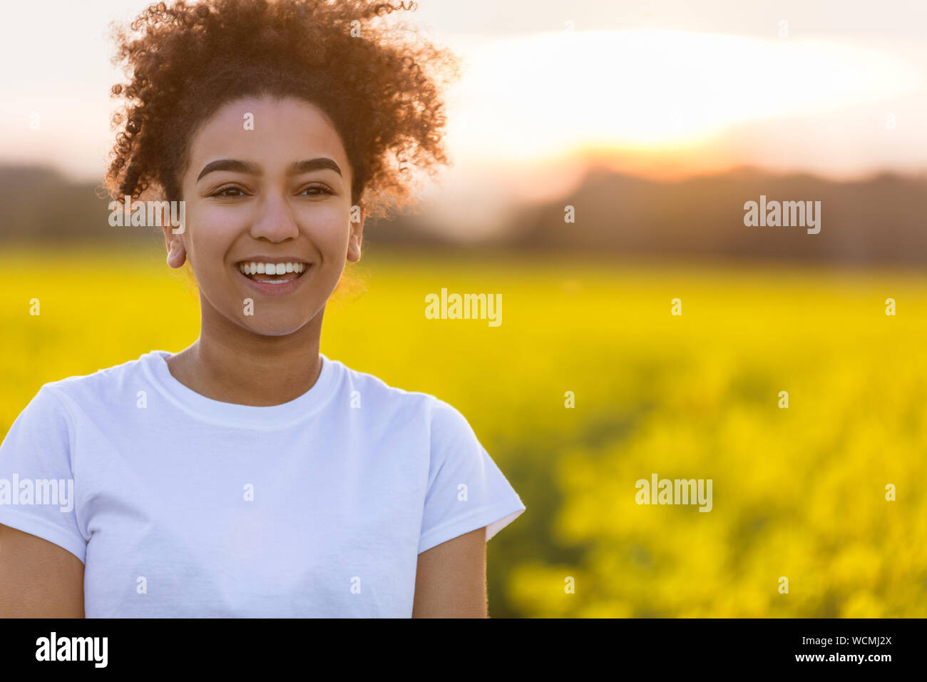 Schönen gemischten Rennen African American Girl Teenager weibliche junge Frau lächelnd und mit perfekter Zähne glücklich in einem Feld von gelben Blumen Stockfoto