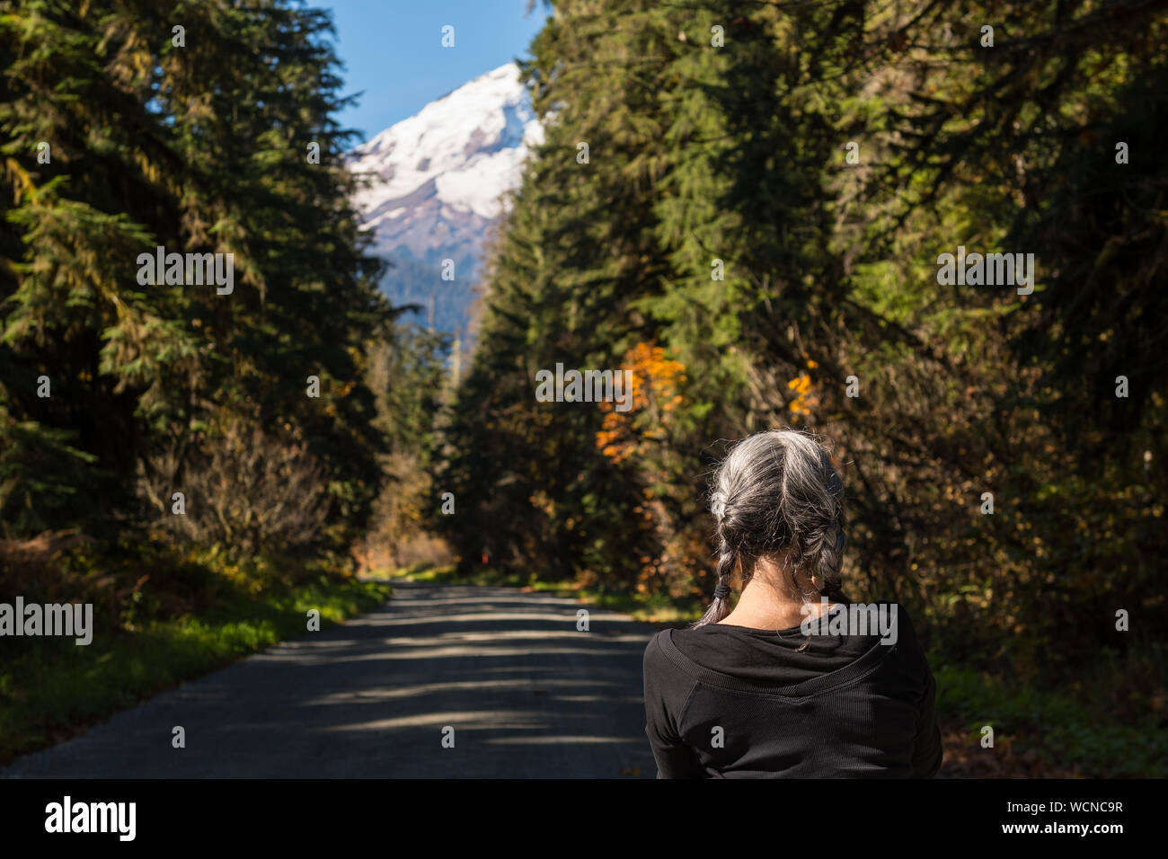 Eine weißhaarige Frau beobachten die Landschaft von Baker Lake Road mit Mount Baker im Hintergrund in North Cascades geschneit Stockfoto